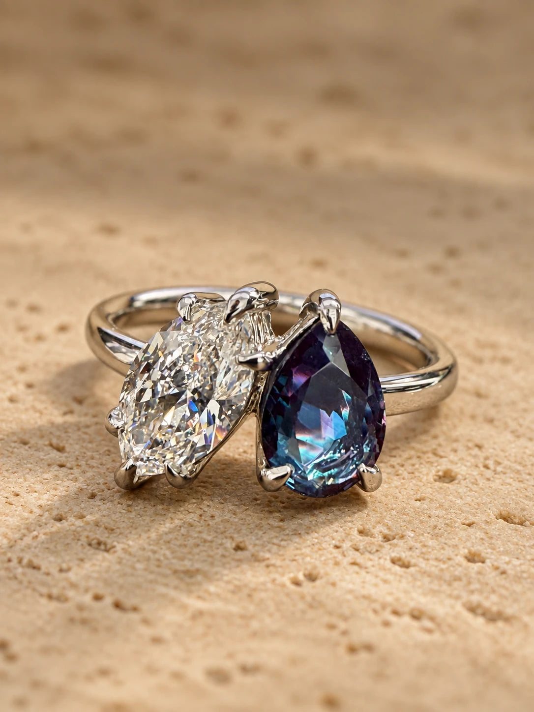 A toi et moi engagement ring in white metal, with a pear-cut alexandrite beside a diamond, on a stone surface