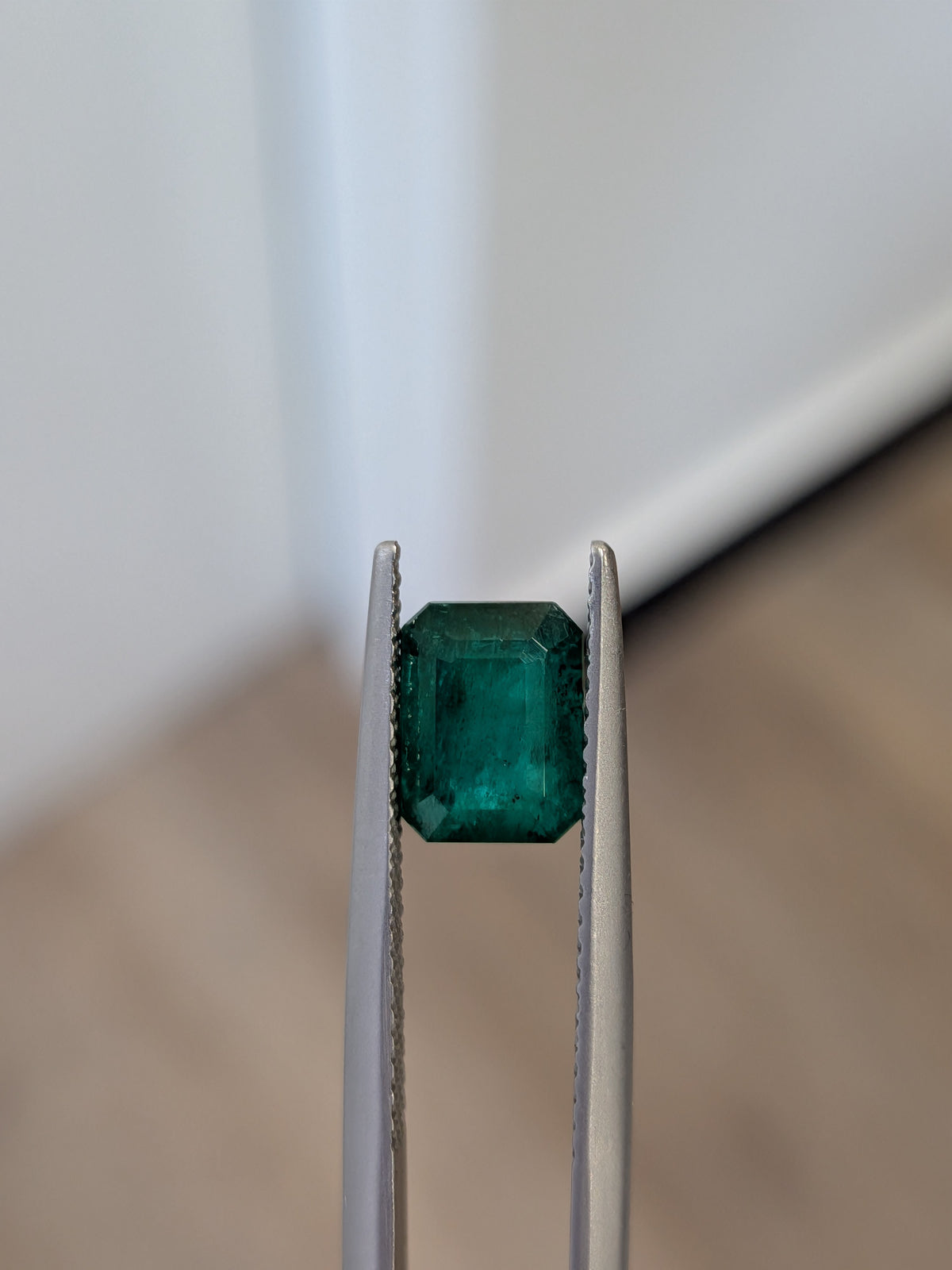 Emerald-cut green gemstone in two metal prongs setting