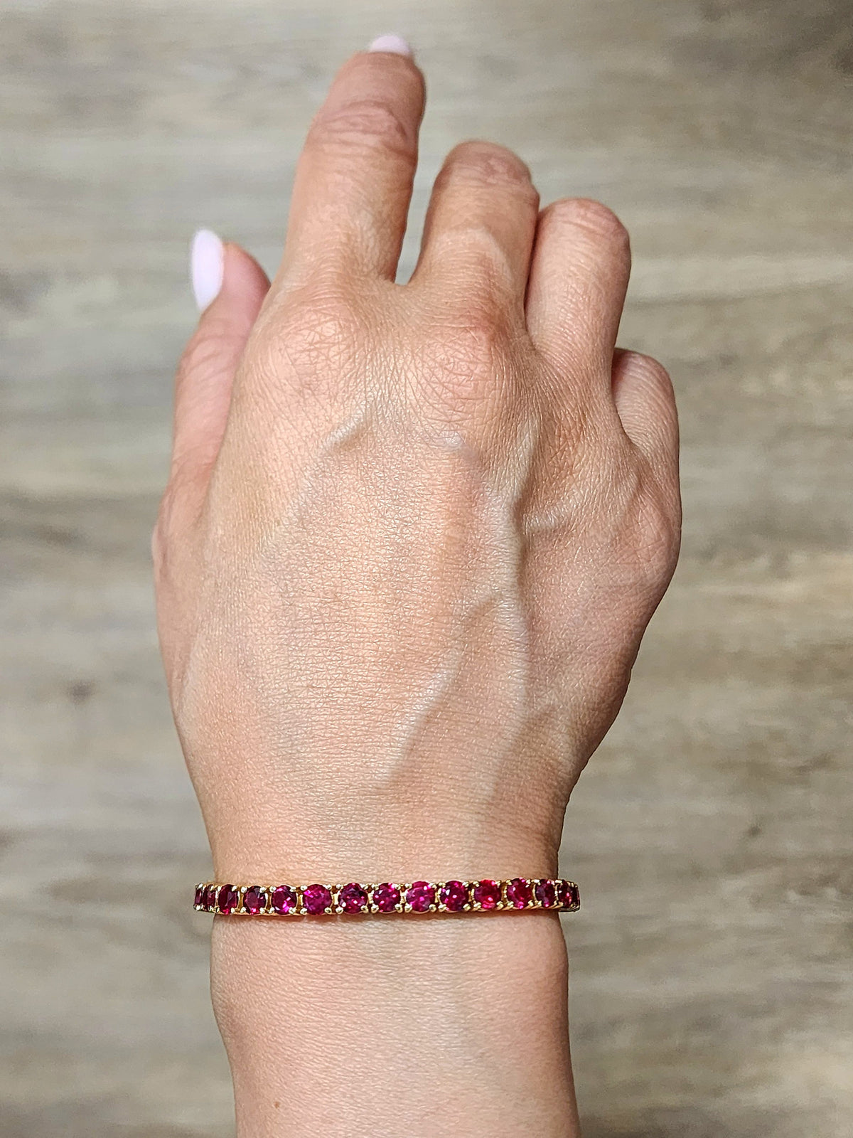 Ruby tennis bracelet on wrist, prong-set round red gemstones in gold-tone setting