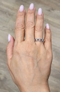 Diamond-lined band ring with dark stones, worn on a hand with light lavender nails.
