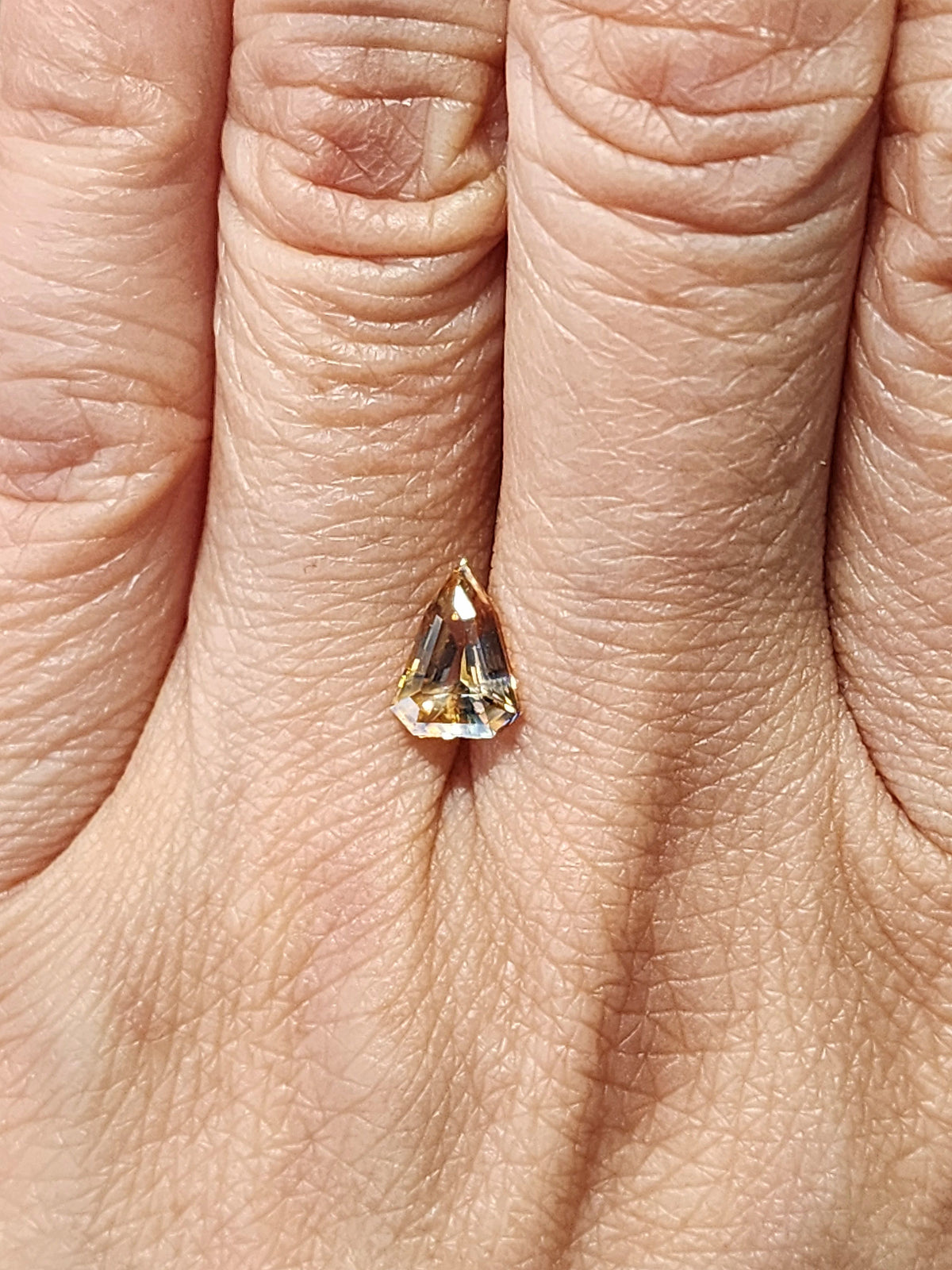 Triangular bi-color sapphire shown on a finger to indicate its small size