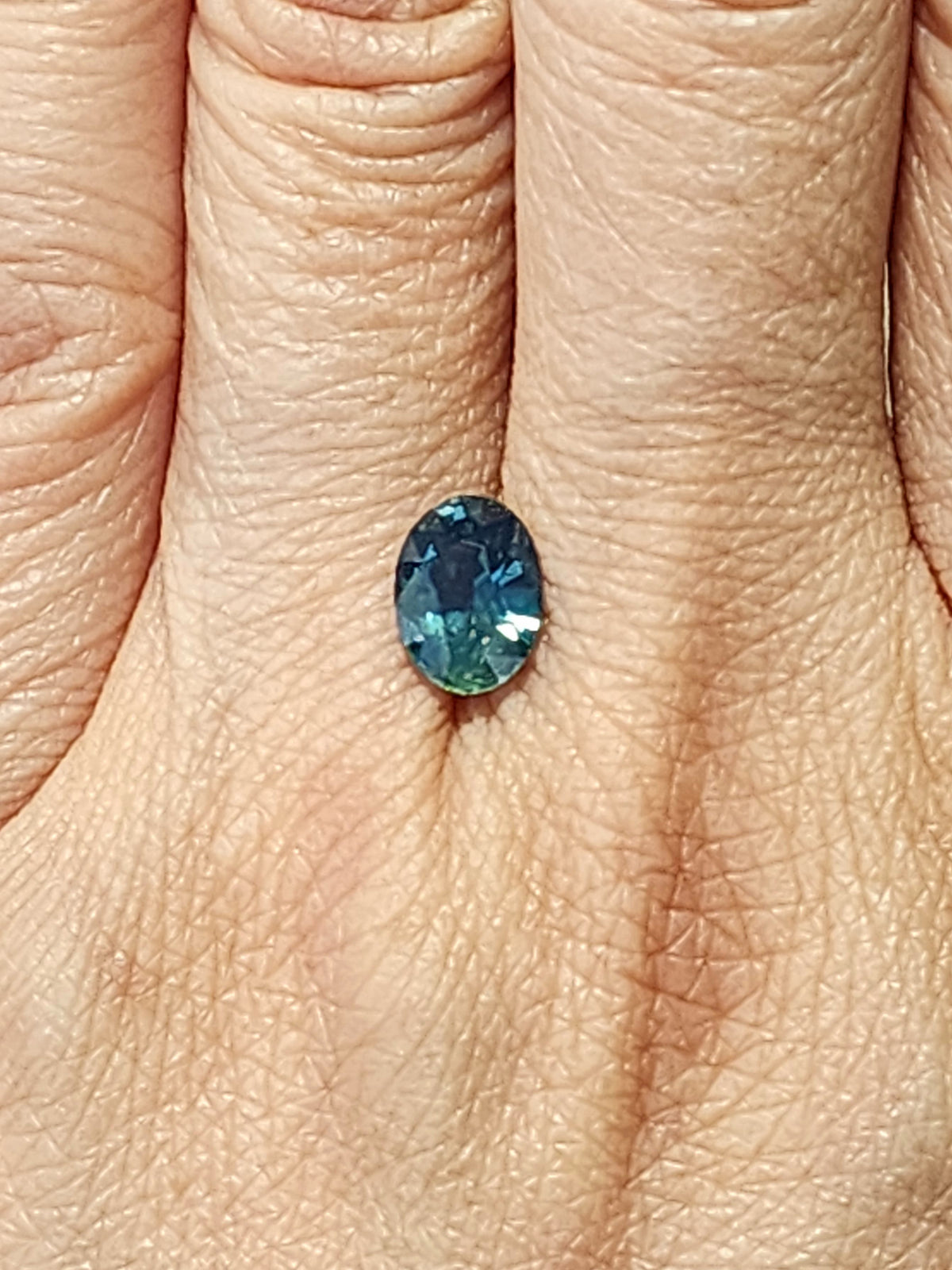 Oval-cut no-heat sapphire shown on a hand for scale