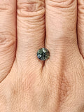 Small round green sapphire shown on a hand for scale