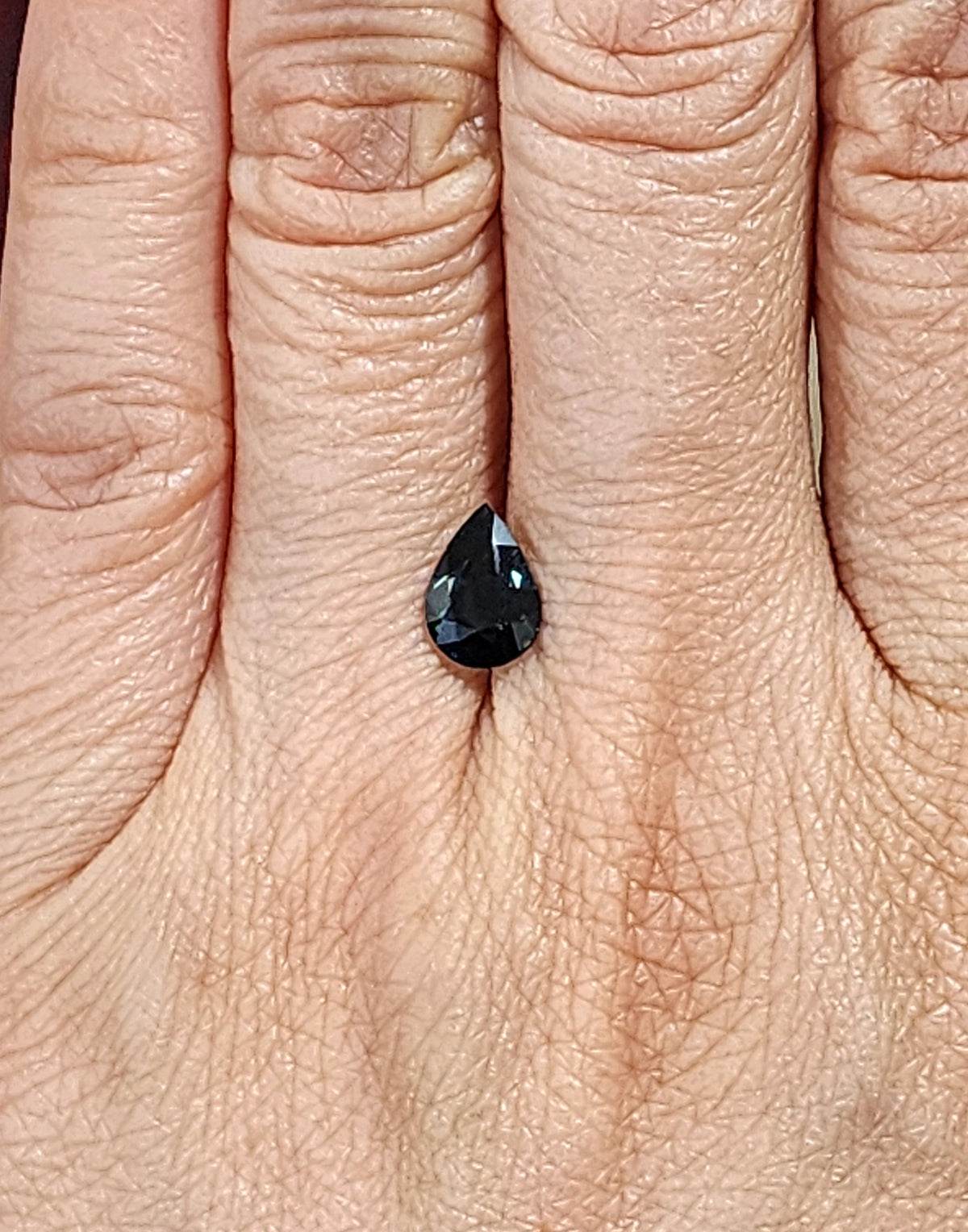 Pear-cut unheated sapphire shown on a hand for scale