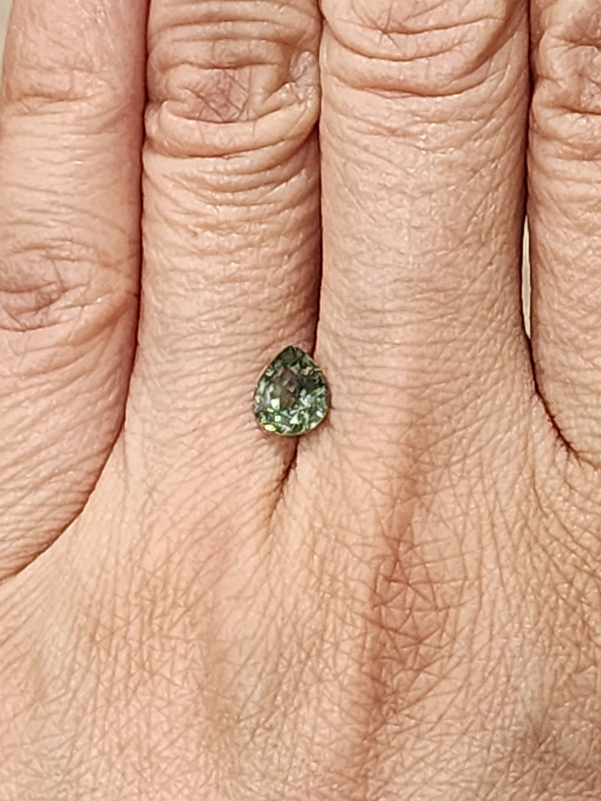 Small pear-cut green demantoid garnet shown on a hand