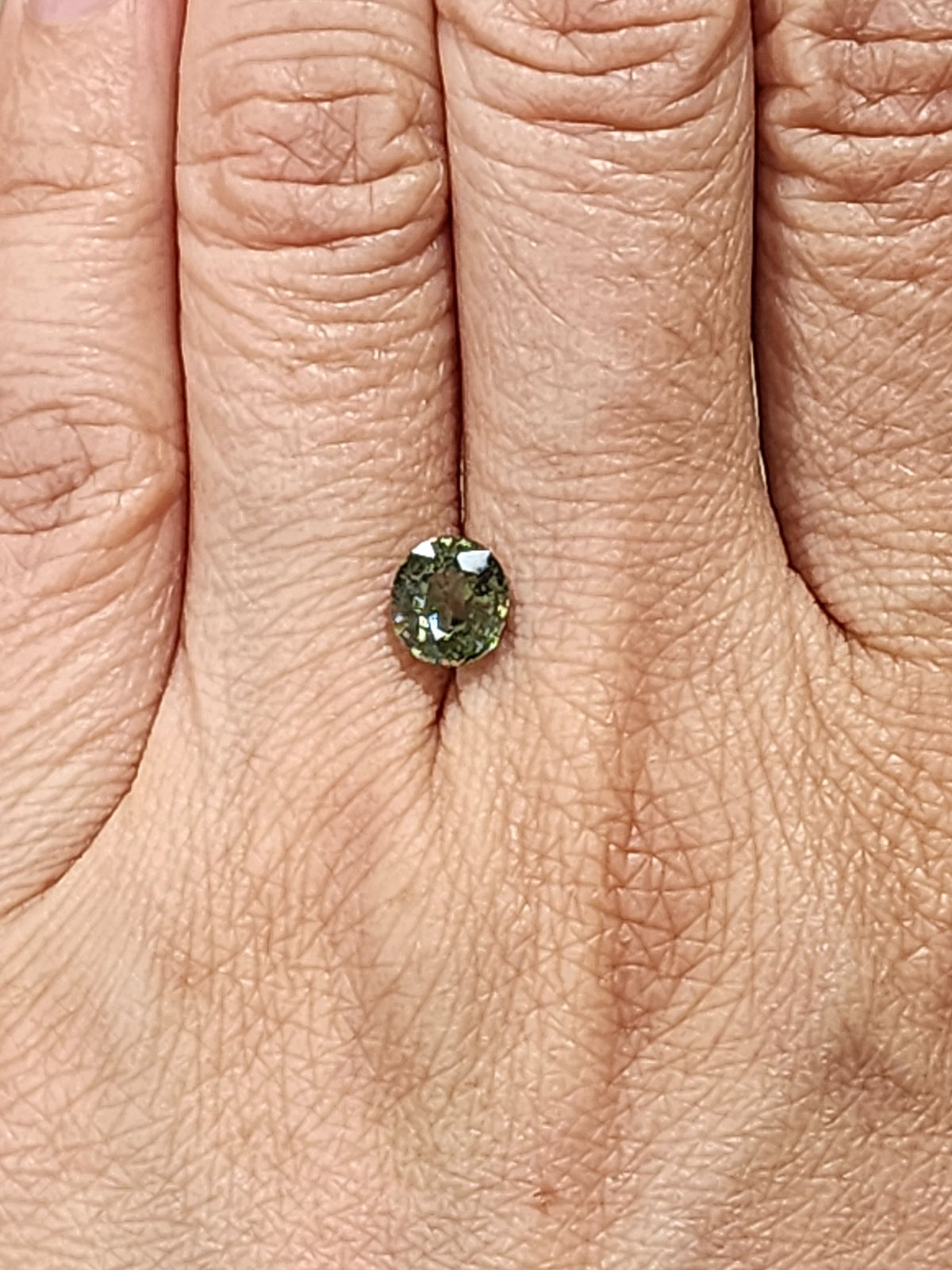 Oval olive green demantoid garnet shown on a hand for scale