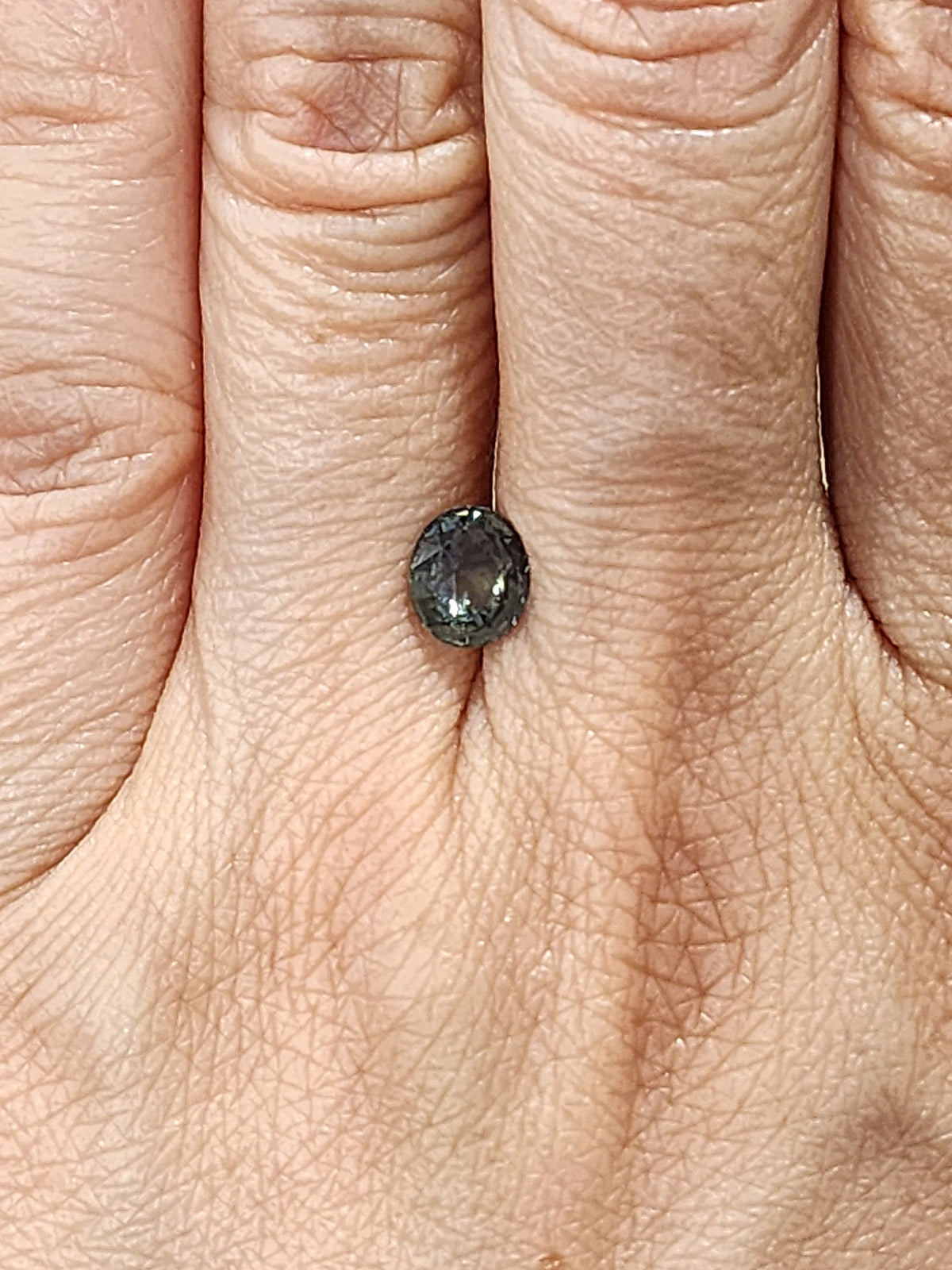 Small oval-cut sapphire shown on a hand, with dark gray-green facets