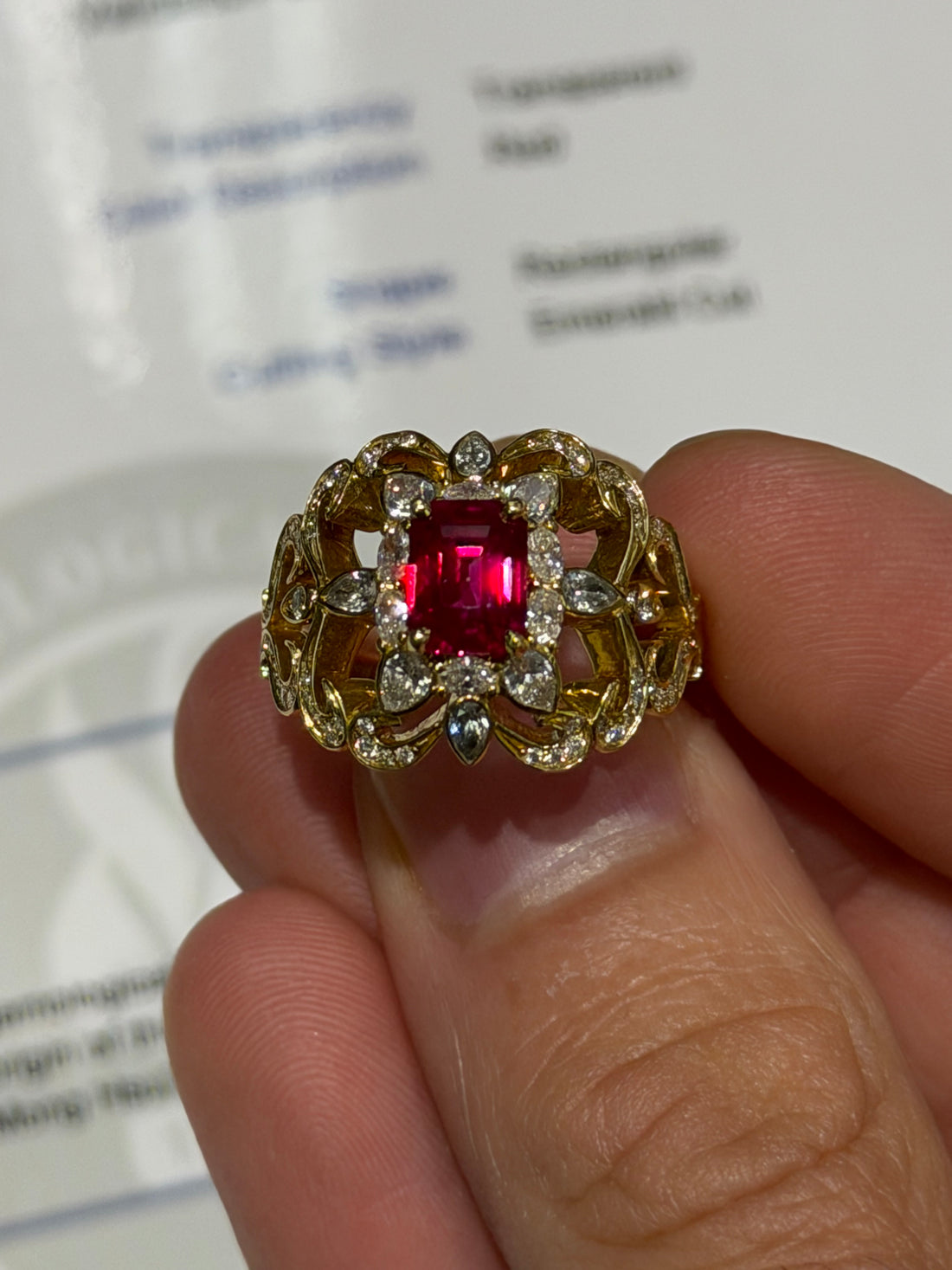 Gold-toned ring with red square ruby center and round clear stones, halo setting