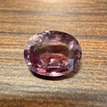 Oval pink sapphire gemstone, faceted oval cut on wood surface