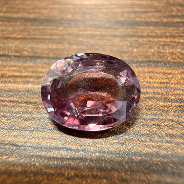 Oval pink sapphire gemstone, faceted oval cut on wood surface