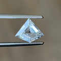 A small triangular clear gemstone held between metal tweezers against a soft beige background.