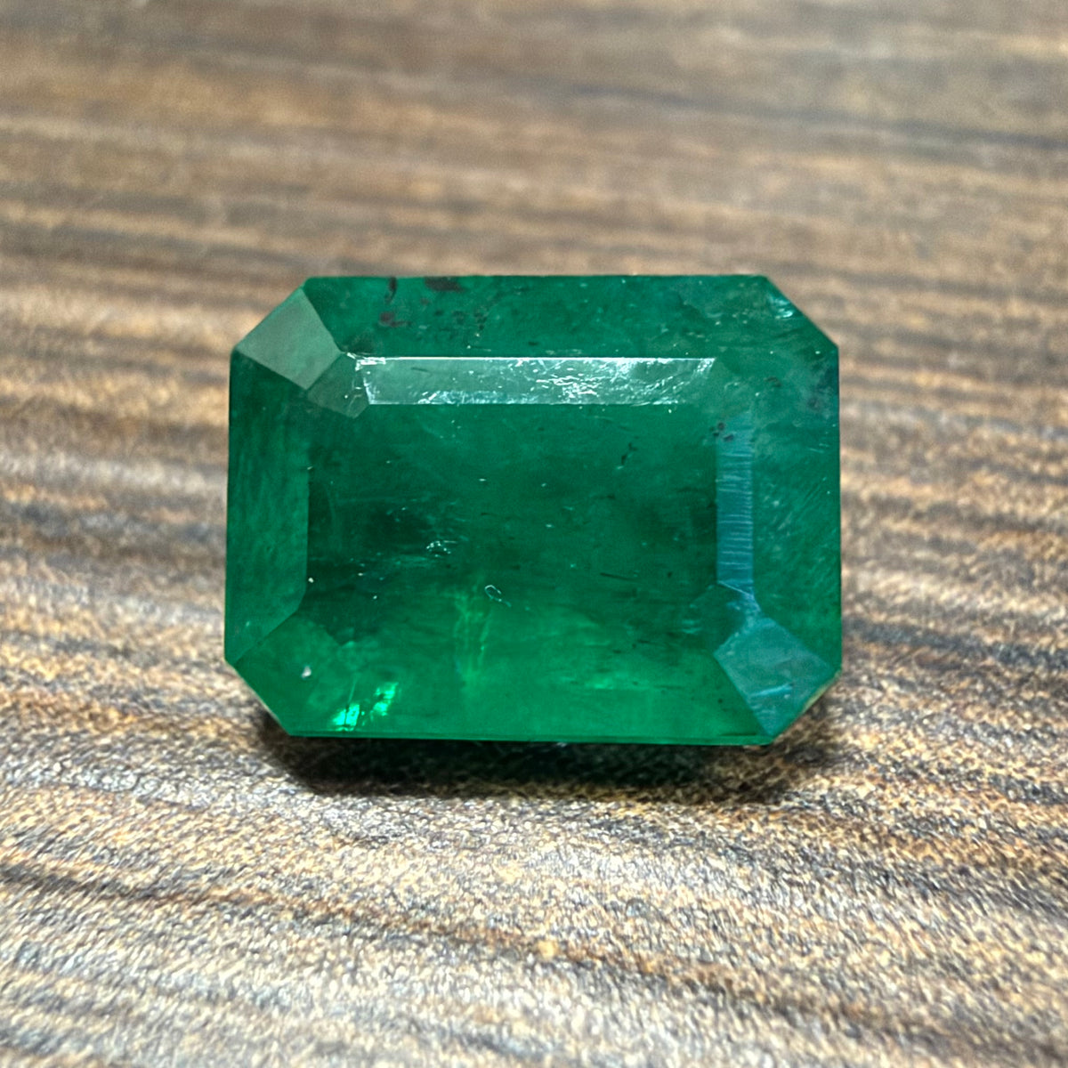 Emerald-cut green gemstone on wooden surface