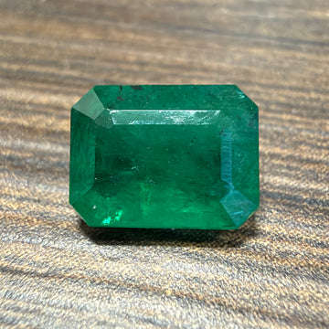 Emerald-cut green gemstone on wooden surface