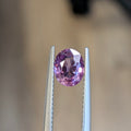 Oval pink sapphire gemstone in silver prongs, faceted oval cut