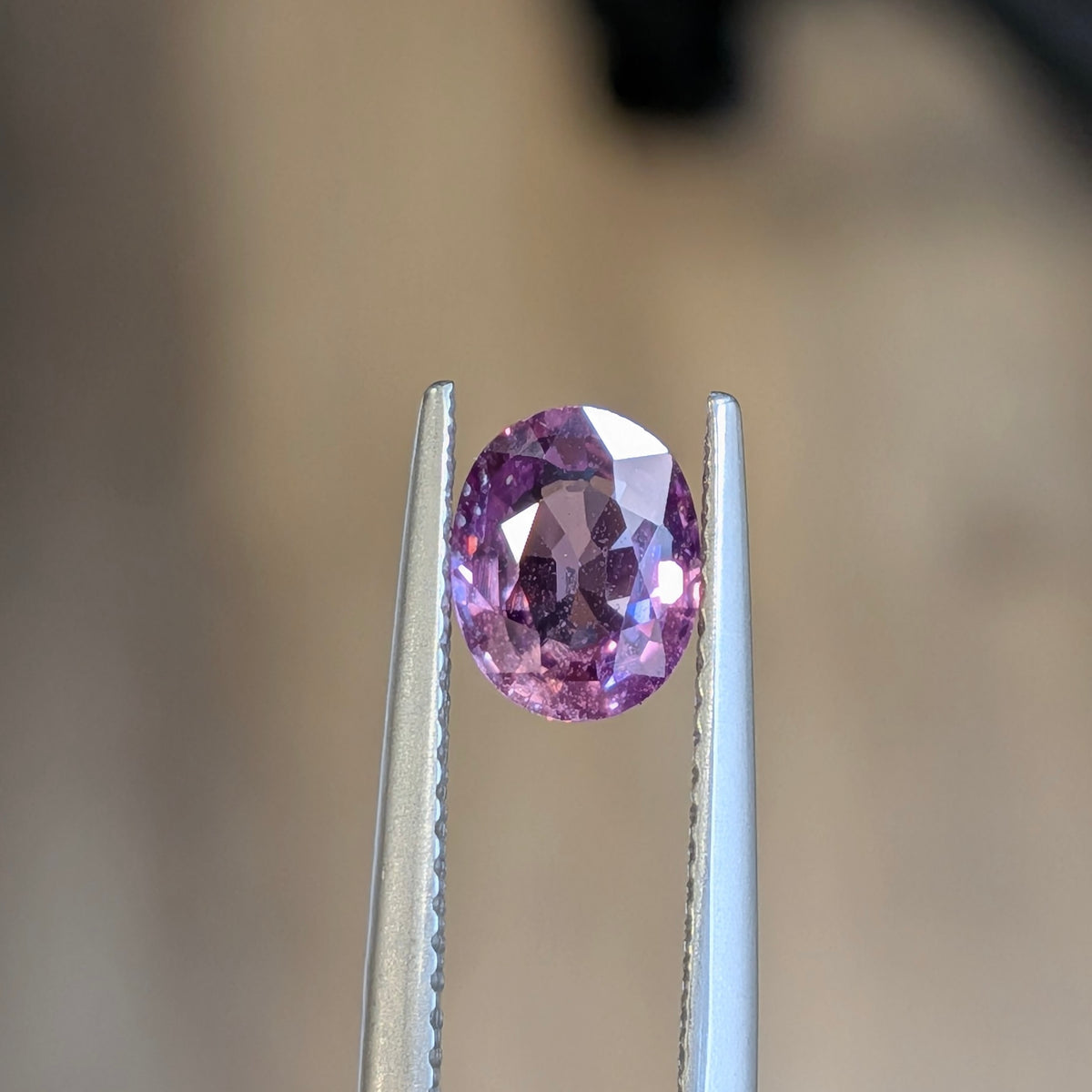 Oval pink sapphire gemstone in silver prongs, faceted oval cut