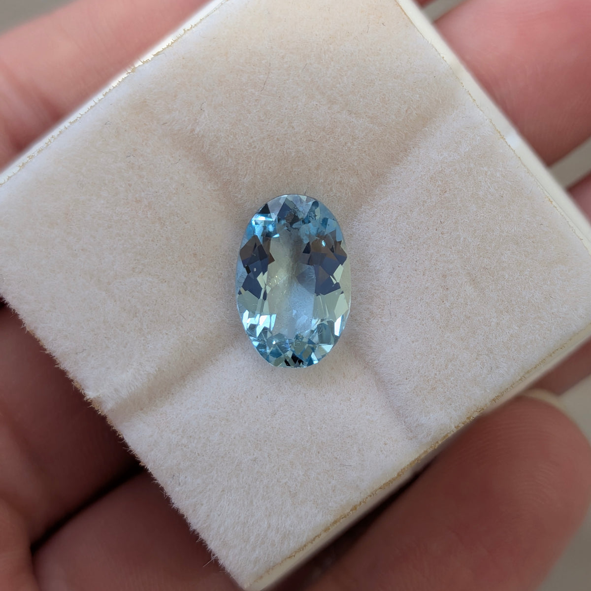 Oval blue aquamarine gemstone on white display pad