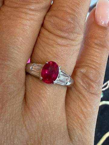 Ruby gemstone ring with baguette diamond accents, oval center, polished silver band.
