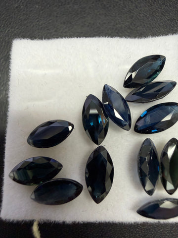 Marquise-cut sapphire gemstones, dark blue, assorted stones on white cloth