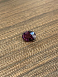 Oval faceted dark purple spinel gemstone on wood surface