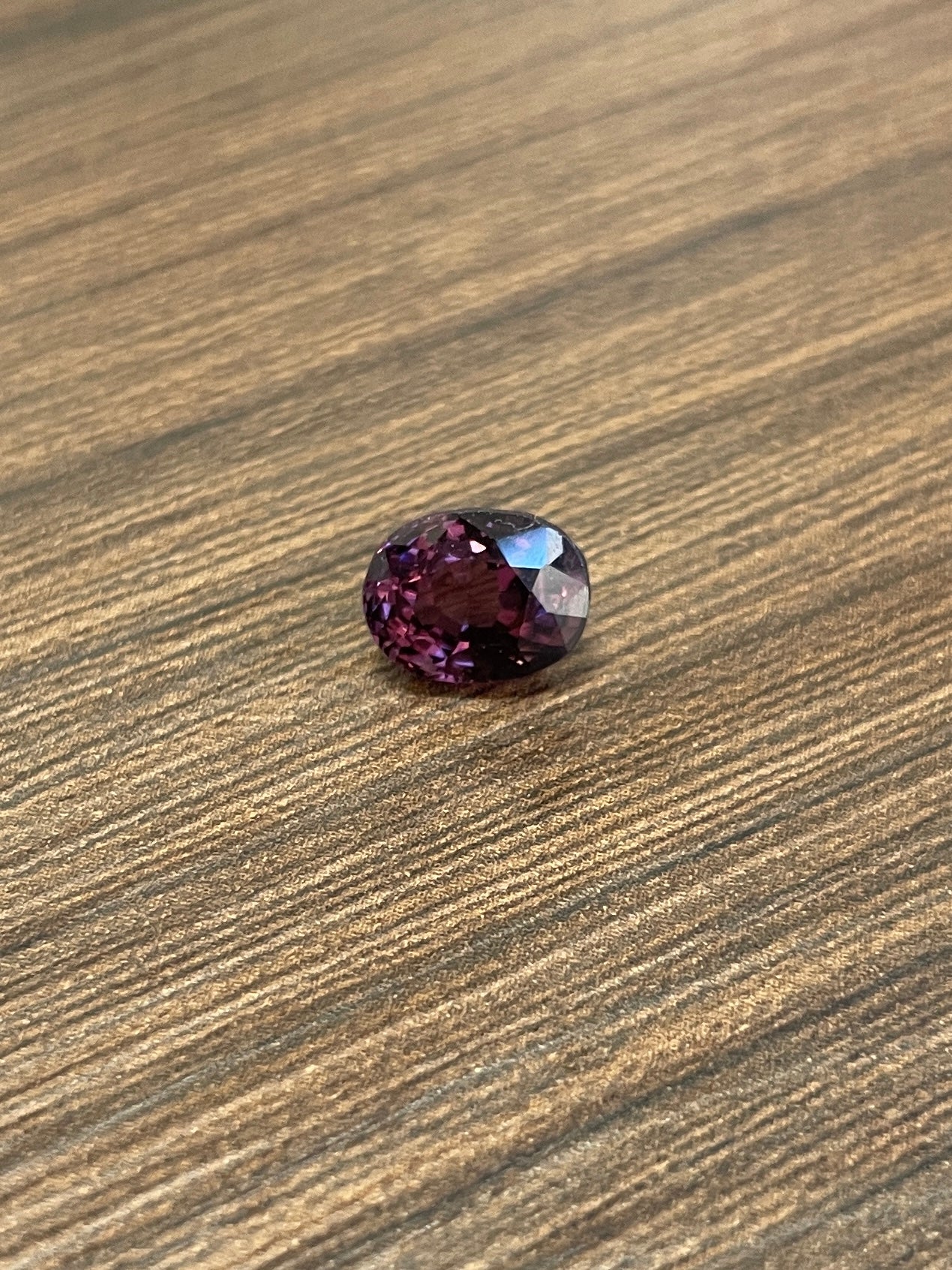 Oval faceted dark purple spinel gemstone on wood surface