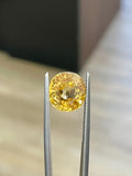 Round yellow zircon gemstone with metal prongs, close-up