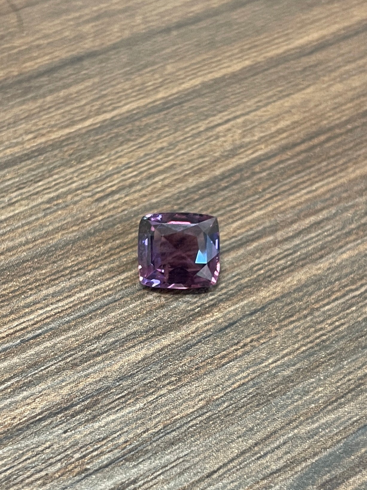 2.45ct purple cushion-cut spinel gemstone on wood surface