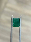 Emerald-cut green gemstone in silver prongs, rectangular step facets