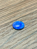 Oval blue boulder opal cabochon gemstone, loose on wood