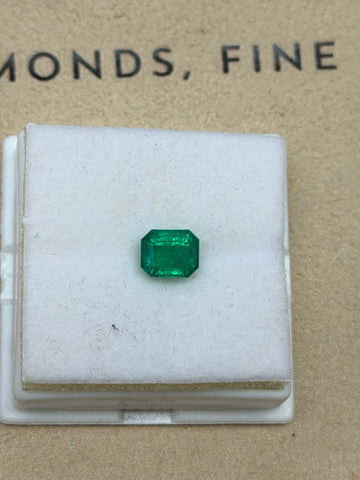 Green emerald-cut gemstone with step facets, set in a white display case