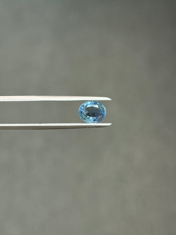 Oval light-blue sapphire gemstone, faceted, close-up held in tweezers