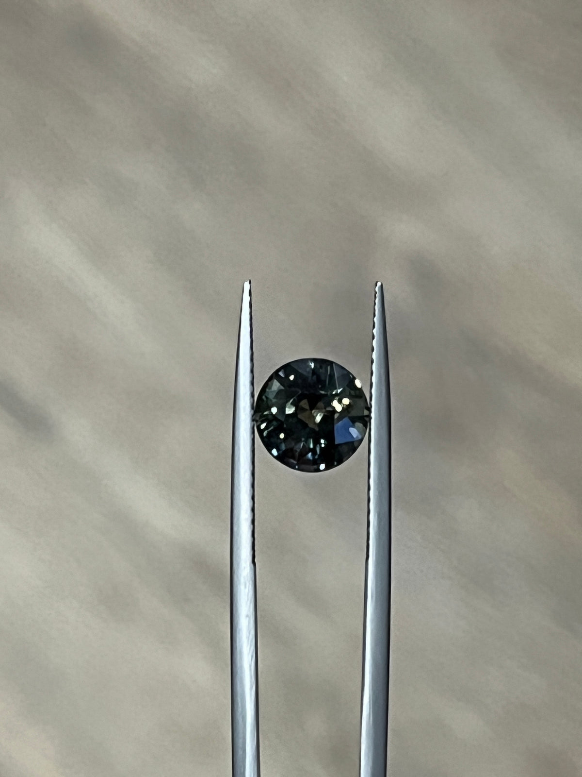 Round dark green sapphire gemstone in a prong setting between two metal posts