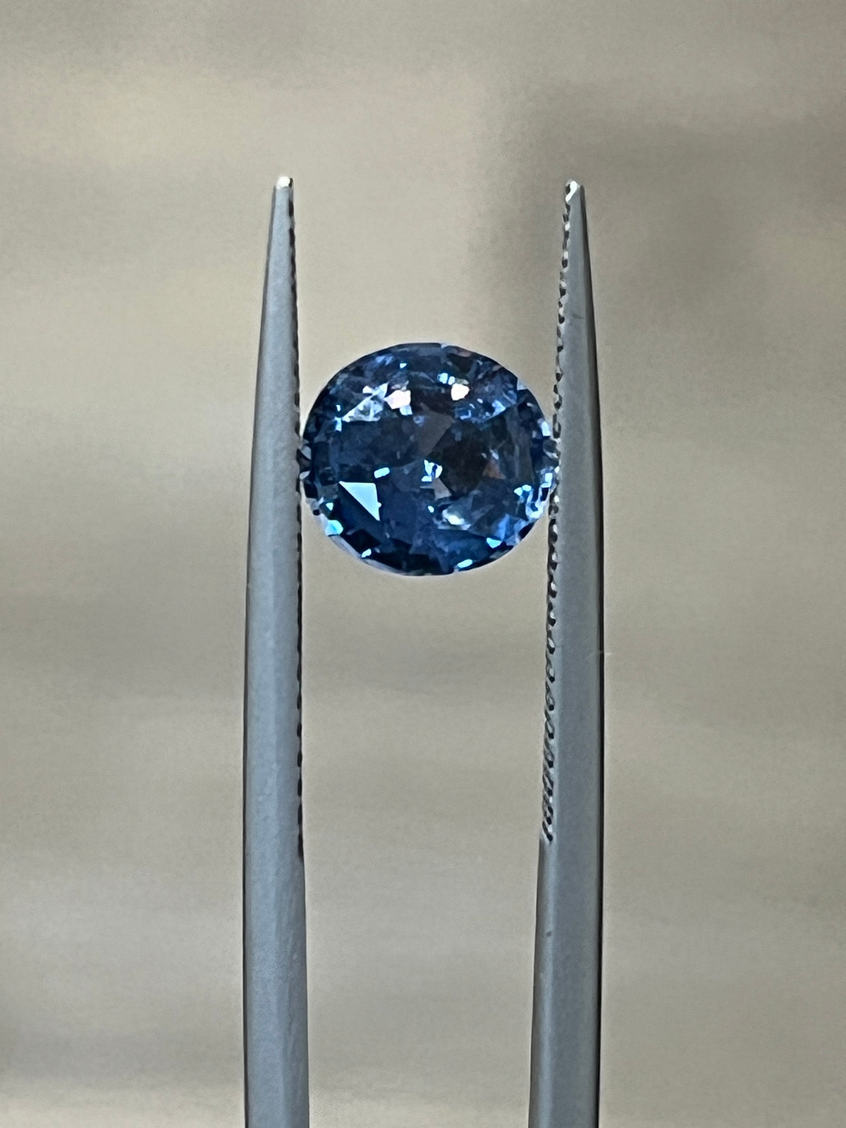 Round blue spinel gemstone held by prongs in a metal setting