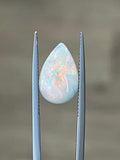 Opal teardrop gemstone held by two metal prongs, displays rainbow play-of-color