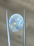 Oval opal cabochon between two metal prongs, iridescent blue-green and gold tones