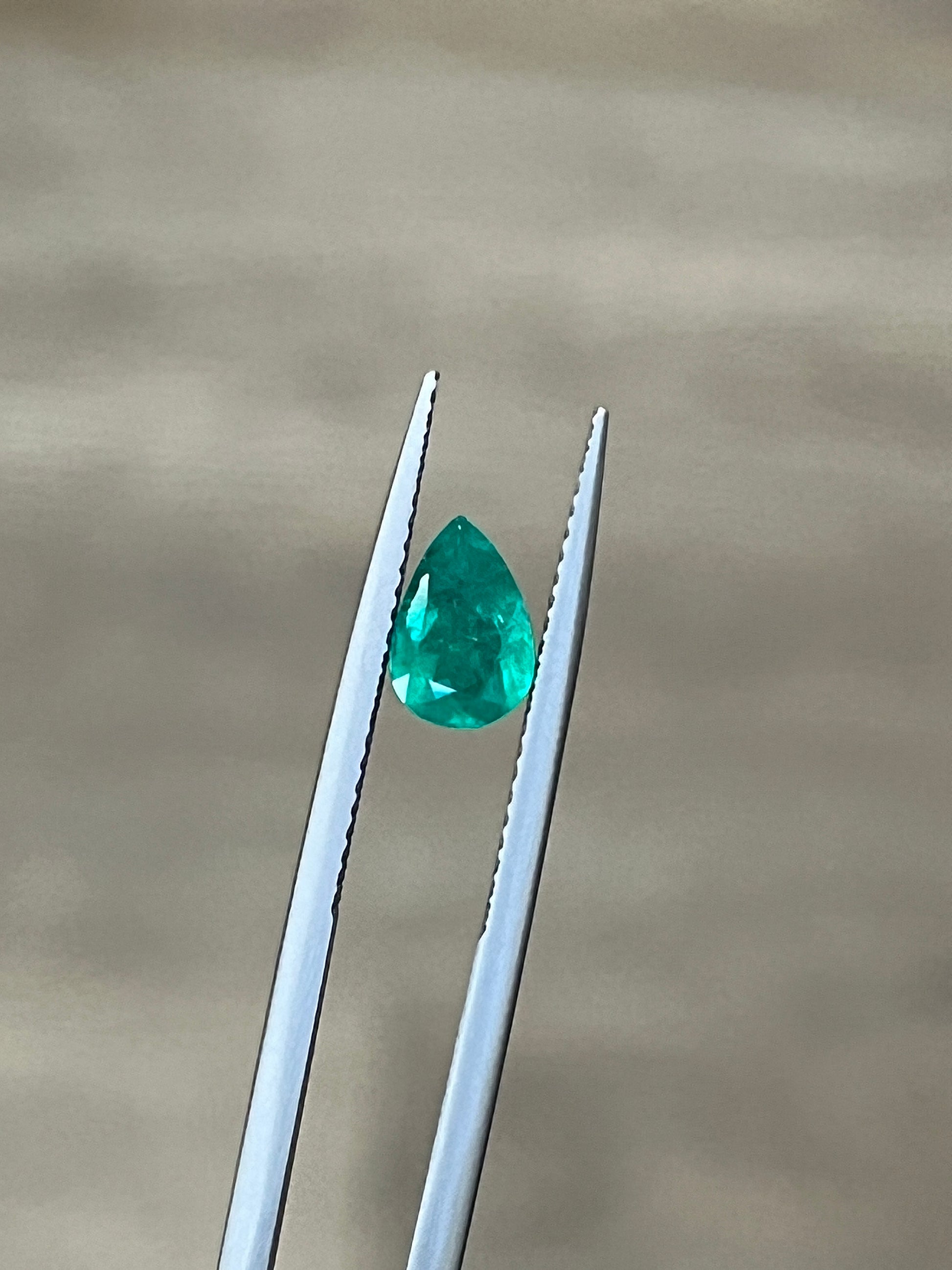 Teardrop emerald gemstone in white metal prongs, bright green