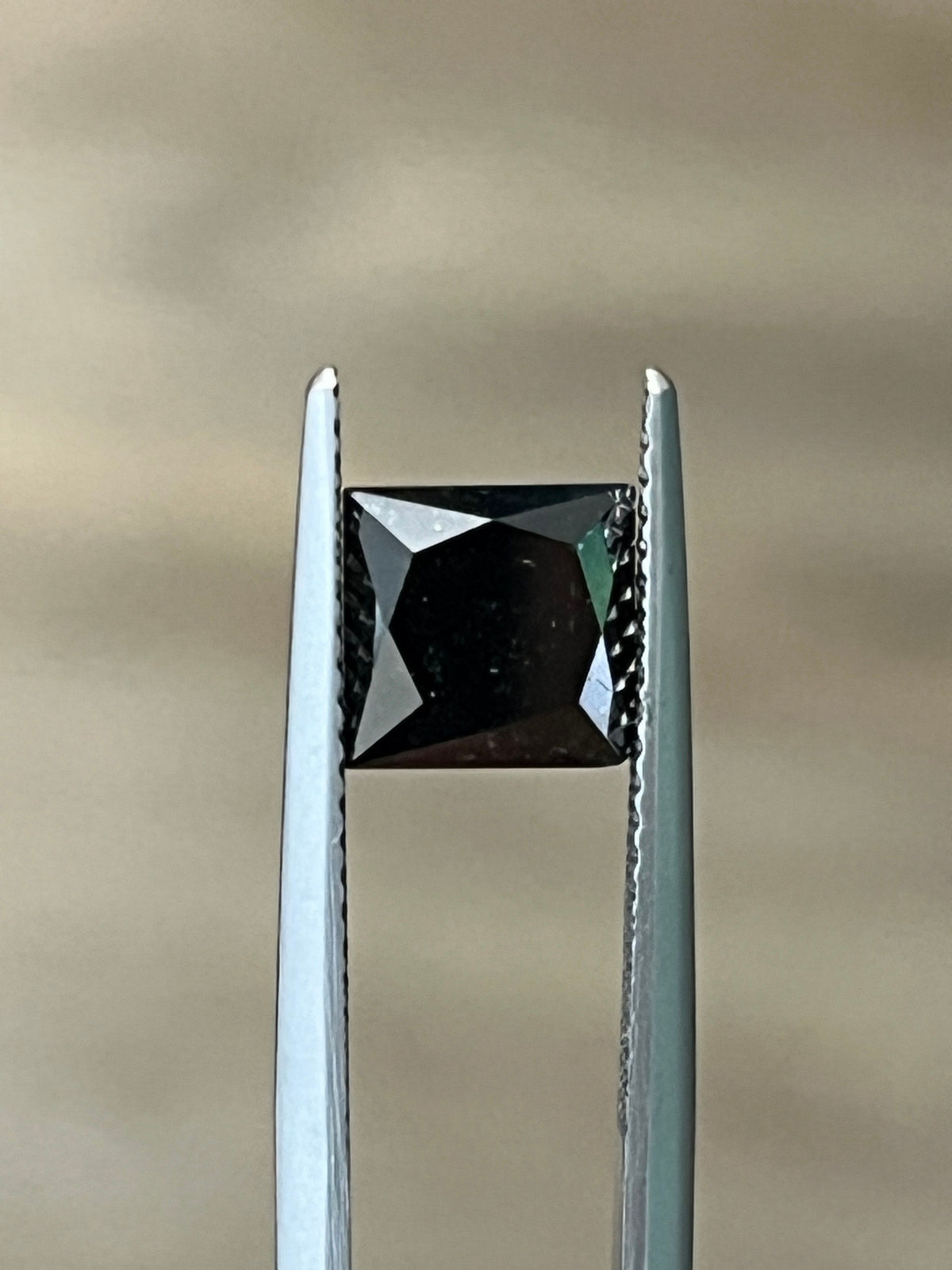 Square black diamond in metal prong setting, angled view