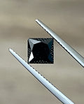 Black cushion-cut diamond held by metal tweezers, visible facets on top