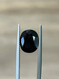 3.10-carat dark gemstone with two metal prongs, oval faceted center