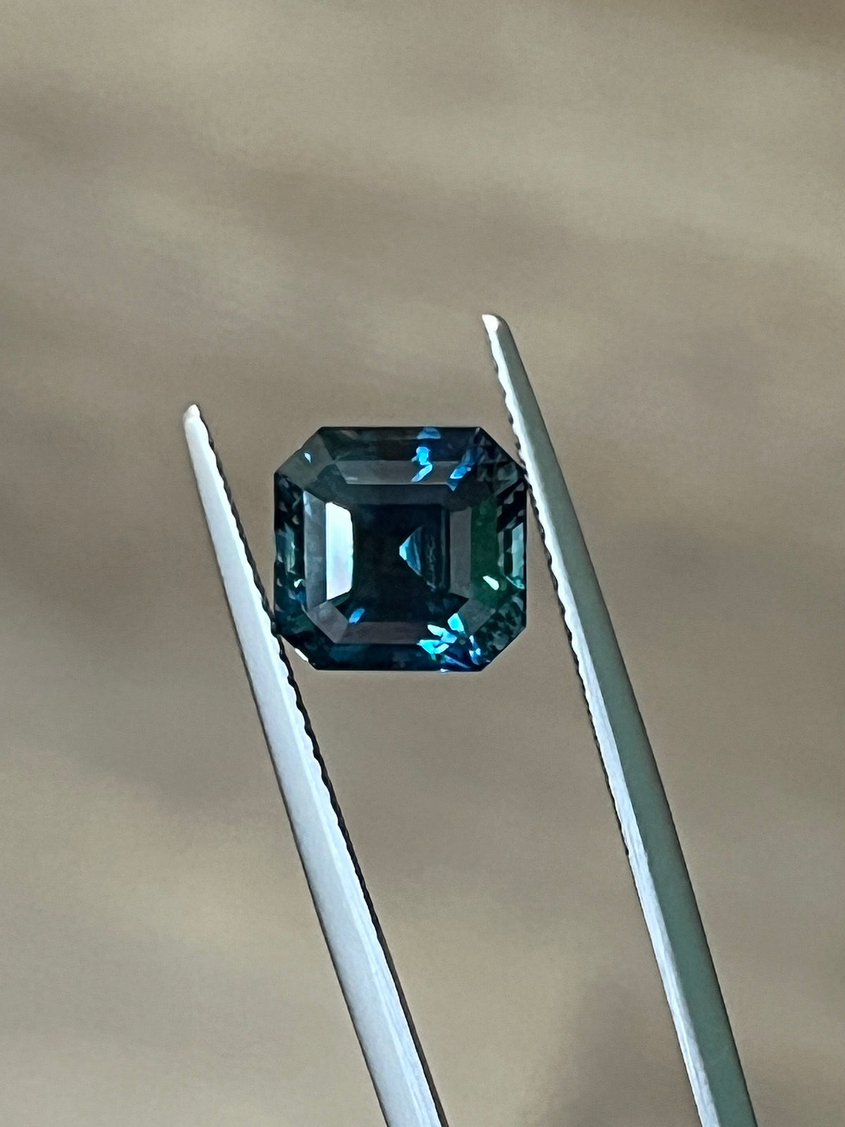 Teal octagonal step-cut sapphire between tweezers