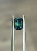 Emerald-cut bi-color sapphire in silver prongs, dark teal with green tones