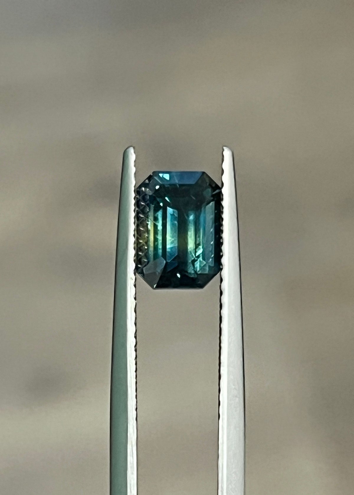 Emerald-cut bi-color sapphire in silver prongs, dark teal with green tones