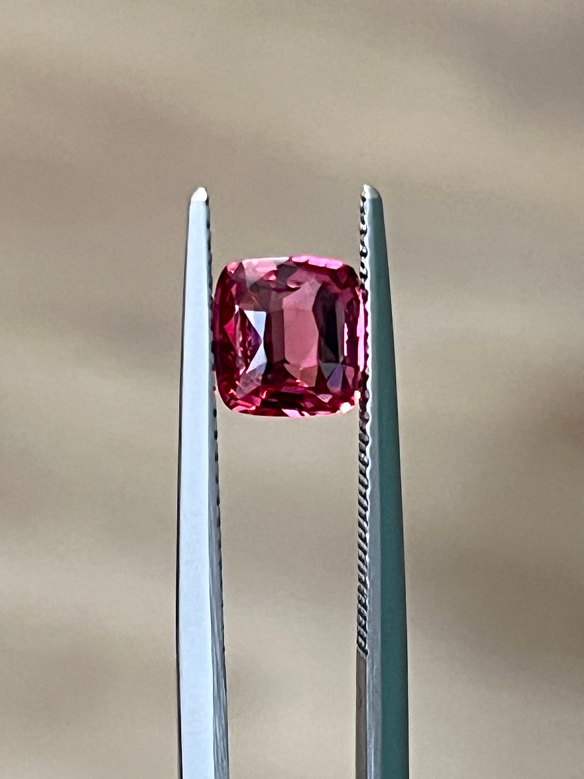 Cushion-cut Mahenge spinel held in jeweler's tweezers, showing its deep pink-red facets