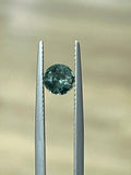 Round faceted green-blue sapphire gemstone held in tweezers