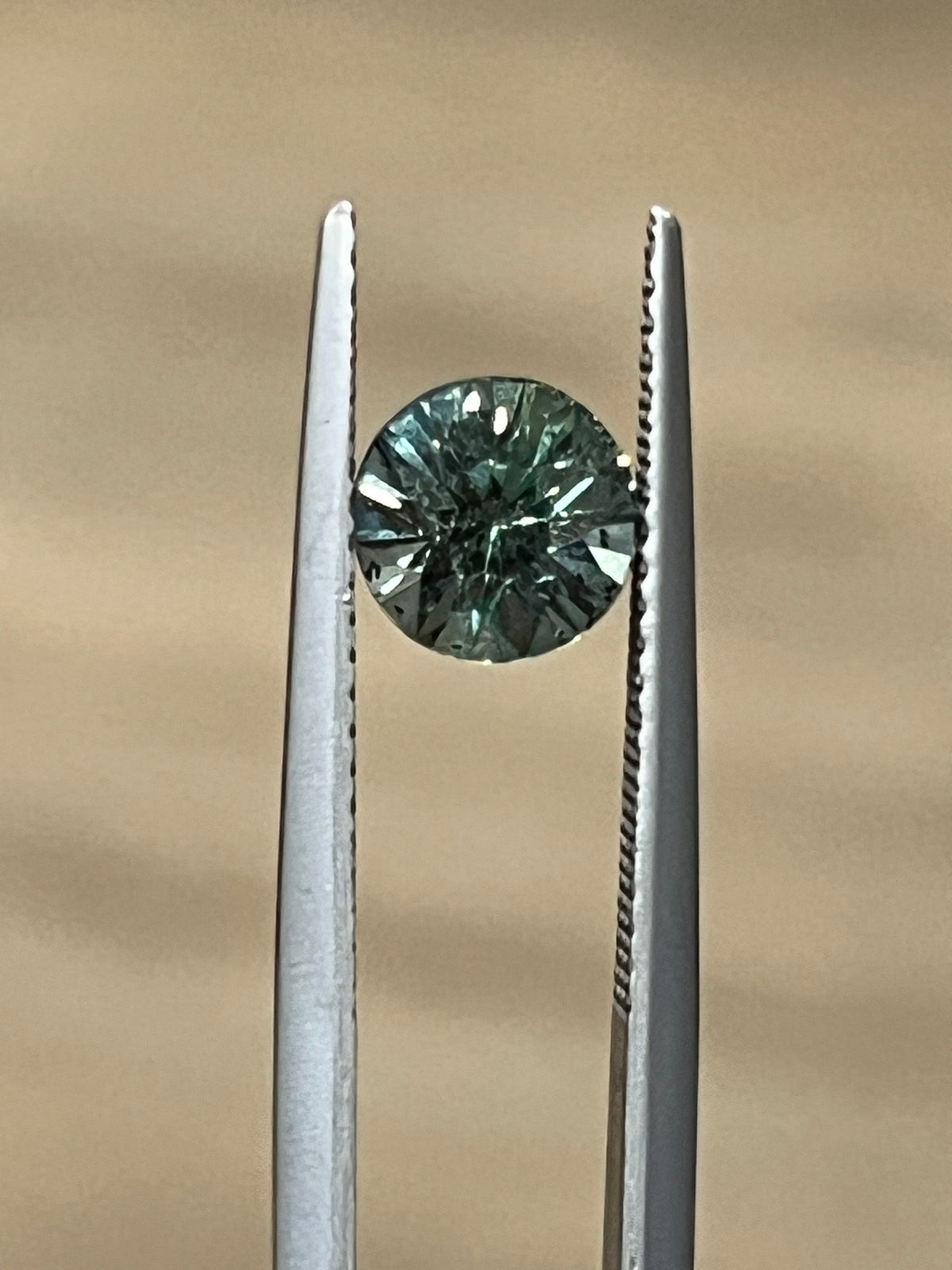Round green sapphire held in tweezers, showing its faceted cut