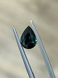 Loose pear-cut unheated sapphire held in tweezers, showing its faceted side