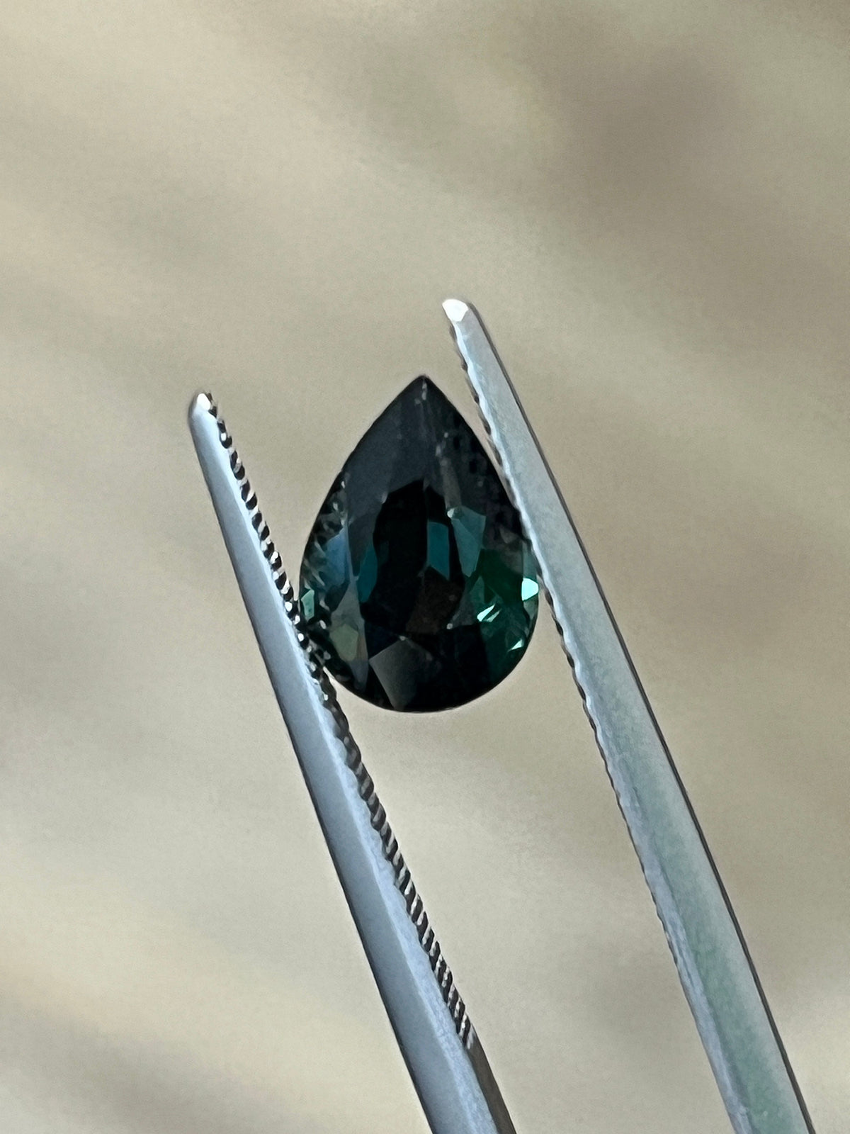 Loose pear-cut unheated sapphire held in tweezers, showing its faceted side