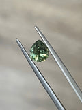 Faceted green demantoid garnet held in gemstone tweezers