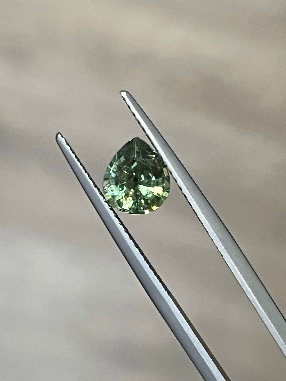 Faceted green demantoid garnet held in gemstone tweezers