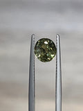 Oval faceted demantoid garnet held in gemstone tweezers