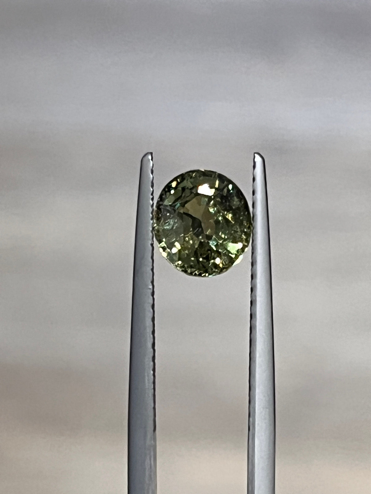 Oval faceted demantoid garnet held in gemstone tweezers